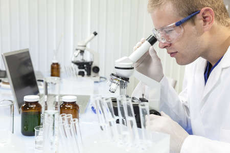 A male medical or scientific researcher or doctor using a microscope in a laboratory with test tubes.の写真素材