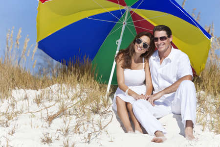 Man and woman romantic couple wearing sunglasses under a multi colored sun umbrella or parasol on a beachの写真素材
