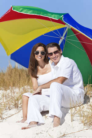 Man and woman romantic couple wearing sunglasses under a multi colored sun umbrella or parasol on a beachの写真素材