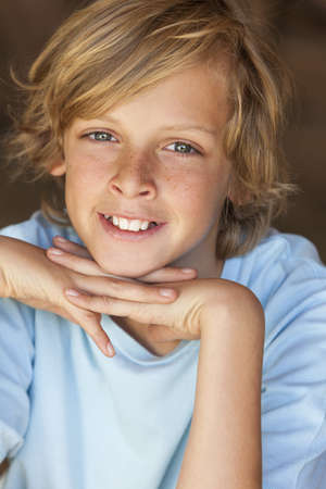 Young happy smiling blond boy child aged about 12 or early teenager resting on his handsの写真素材