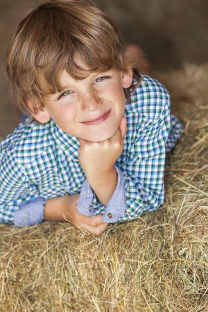 Young happy smiling boy wearing a plaid shirt and laying on bales of hay or strawの写真素材