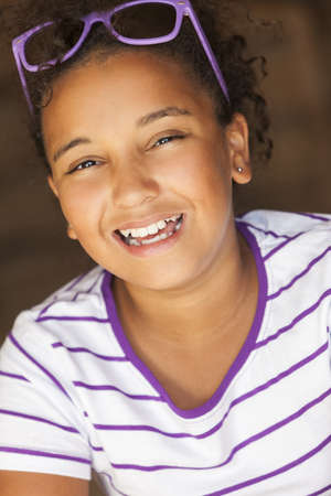 A beautiful and happy smiling mixed race African American female girl child wearing sunglasses in golden sunshine and laughingの写真素材