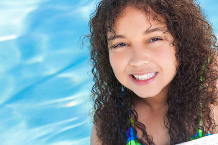 A cute happy young interracial African American girl child relaxing on the side of a swimming pool smilingの写真素材