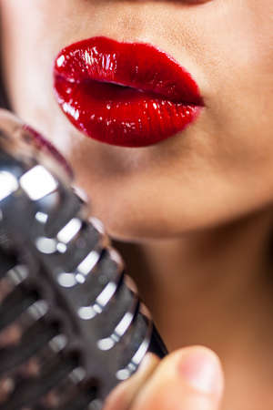 Close up of beautiful female woman singer mouth with red lips singing into a vintage microphoone in a night clubの写真素材
