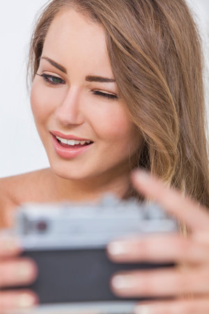 A beautiful shirtless blond girl or young woman winking and taking a selfie picture on a retro style digital cameraの写真素材