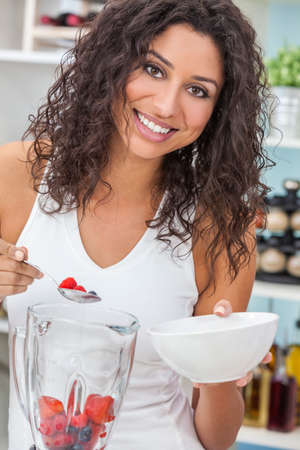 A beautiful happy young woman or girl making a fresh fruit smoothie in her kitchen at homeの写真素材