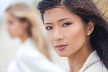 Outdoor profile portrait of a beautiful thoughtful Chinese Asian young woman or girl with blond female friend at beachの写真素材