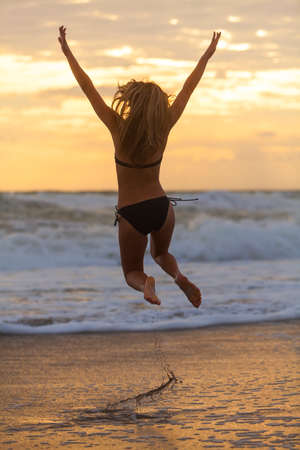 Happy young woman girl in bikini jumping on a beach at sunset or sunriseの写真素材