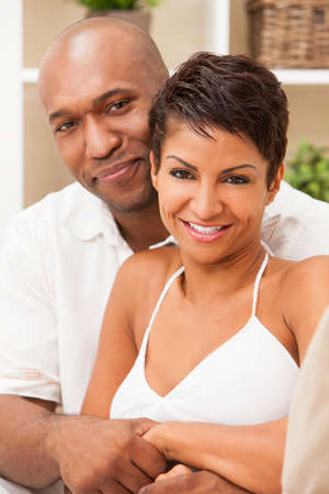 A happy African American man and woman couple in their thirties sitting at home, the woman is in focus in the foreground the man out of focus in the background. A happy African American man and woman couple in their thirties sitting at home, the woman is in focus in the foreground the man out of focus in the background.