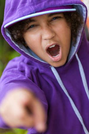 Young African American girl female child wearing hoody hoodie & baseball cap shouting and pointing to cameraの写真素材