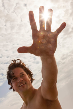 Young Asian man reaching for sun flare on vacation beach