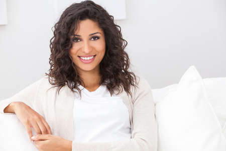 Portrait of a beautiful young Latina Hispanic woman smiling with perfect teeth sitting on a white sofa