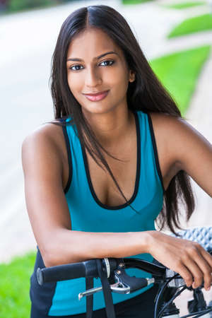 Outdoor fitness portrait of a beautiful Indian Asian young woman or girl outside in summer sunshine riding cycling her bicycleの写真素材