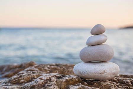 Tower of stones piles on top of a rock on a tranquil deserted beach at evening sunsetの写真素材