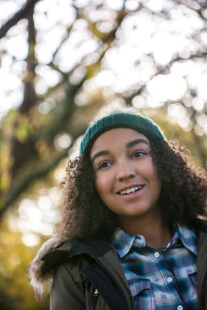 Beautiful happy mixed race African American teenager girl in autumn or fall forest treesの写真素材