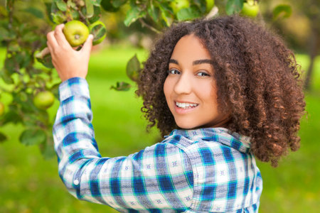 Outdoor portrait of beautiful happy mixed race African American girl teenager female child picking...