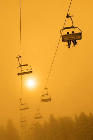 People on ski chair lift at misty sunset or sunriseの写真素材