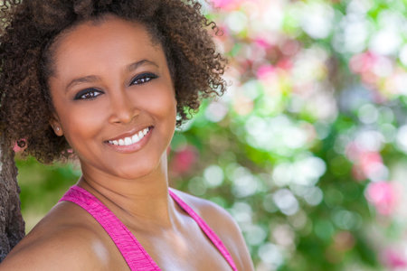 Beautiful young mixed race black African American woman with perfect teeth smiling and relaxing outside in summer sunshineの写真素材