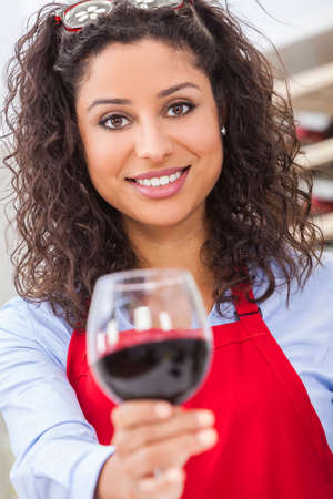 A beautiful latina hispanic girl or young woman drinking red wine at home toasting to cameraの写真素材
