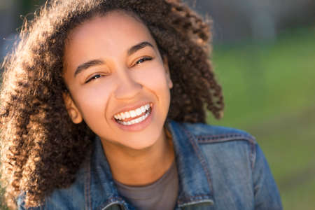 Outdoor portrait of beautiful happy mixed race African American girl teenager female young woman smiling laughing with perfect teethの写真素材