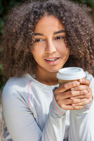 Beautiful happy mixed race African American girl teenager female young woman smiling drinking takeaway coffee outsideの写真素材