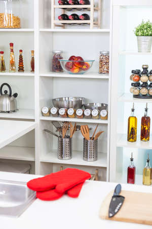 A modern kitchen empty no people, with red oven gloves, oils, olive oil, wine, fruit, spices, equipment, utensils, kettle, knife and chopping boardの写真素材