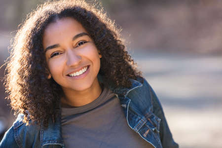 Outdoor portrait of beautiful happy mixed race African American girl teenager female young woman smiling laughing with perfect teethの写真素材