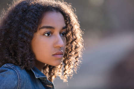 Beautiful mixed race African American girl teenager female young woman outside by a road looking sad depressed or thoughtfulの写真素材
