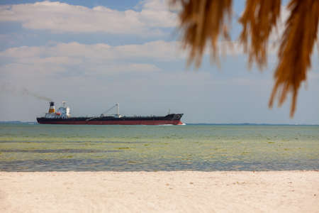 Oil tanker sailing past empty tropical beach with palm tree and white sandの写真素材