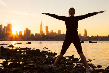 Silhouette of a young woman or girl exercising at sunrise in front of the New York City Skylineの写真素材