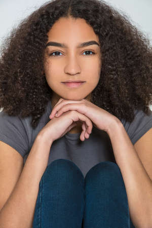 Studio shot of a beautiful African American mixed race interracial teenager girl young woman smiling and resting on her handsの写真素材