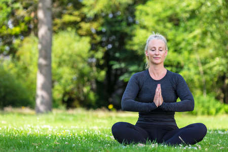 Mature middle aged fit healthy woman practicing yoga outside in a natural tranquil green environment