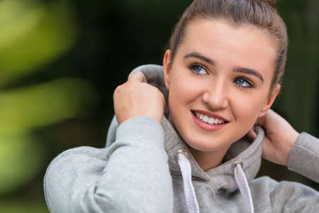 Happy pretty teenage female girl young woman with blue eyes and perfect teeth, smiling and wearing hoody outside in spring or summerの写真素材
