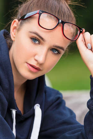Pretty intelligent girl or young woman wearing glasses and lifting them to show her blue eyesの写真素材