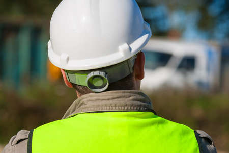 Rear view of construction worker on a building site and dressed in safety clothing of hard hat and high visibilty vestの写真素材