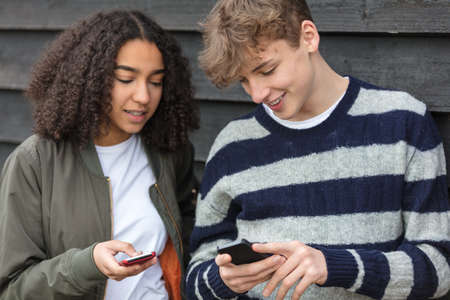 Interracial teenagers boy and girl, male and female, mixed race African American girl, Caucasian boy,  texting and using mobile cell phoneの写真素材