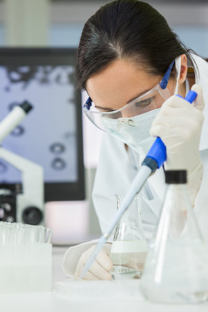 A female medical or scientific researcher or scientist using a pipette, flask and test tubes in a...