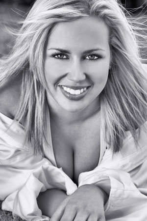 Black and white photograph of beautiful blond haired model with perfect teeth, wearing a white shirt shot outside using natural lightの写真素材