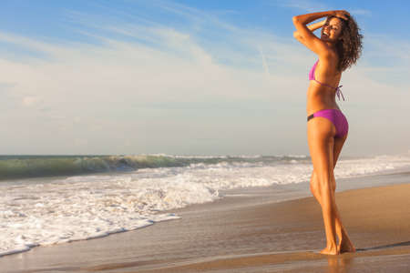 Beautiful young woman in bikini with sun tan in sunshine on a deserted tropical beach with blue skyの写真素材