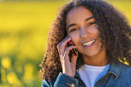 Outdoor portrait of beautiful happy mixed race African American girl teenager female young woman Talking on cell phone and smiling with perfect teethの写真素材