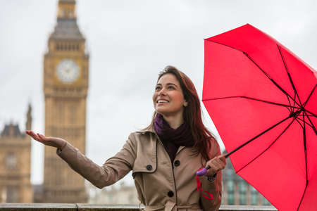 Girl or young woman with a red umbrella, hand out, checking for rain by Big Ben, London, England, Great Britainの写真素材