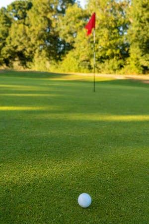 Golf ball, hole and red flag on the green of a golf courseの写真素材
