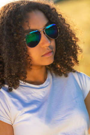Beautiful mixed race African American female girl teenager young woman wearing reflective blue aviator sunglasses at at sunset or sunriseの写真素材