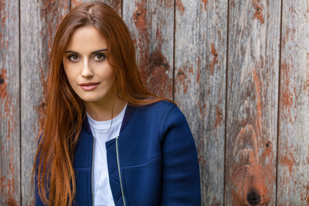 Outdoor portrait of beautiful girl or young woman with red hair wearing a ble jacket and white...