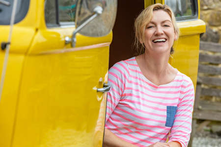 Portrait shot of an attractive, successful and happy middle aged woman laughing sitting in the doorway of a camper van busの写真素材