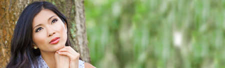Web banner panoramic outdoor portrait of a beautiful young Chinese Asian young woman or girl with natural green backgroundの写真素材