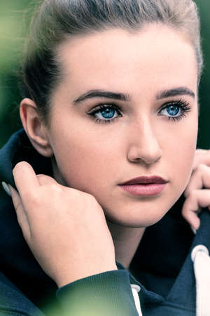 Beautiful girl teenager female young woman with blue eyes outside wearing dark blue hoody looking sad depressed or thoughtfulの写真素材