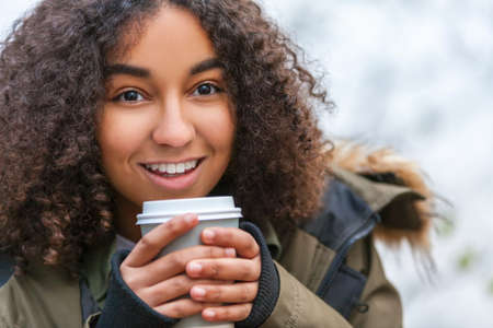 Beautiful happy mixed race African American girl teenager female young woman smiling drinking takeaway coffee outsideの写真素材