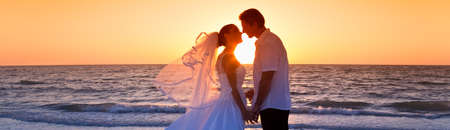 Married couple, bride and groom, kissing at sunset at a beautiful tropical beach wedding panoramic web bannerの写真素材