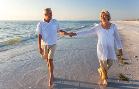 Happy senior man and woman couple walking and holding hands on a deserted tropical beach with bright clear blue skyの写真素材